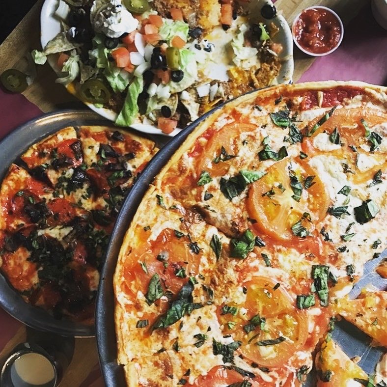 Pizza slices beside heros and pasta.